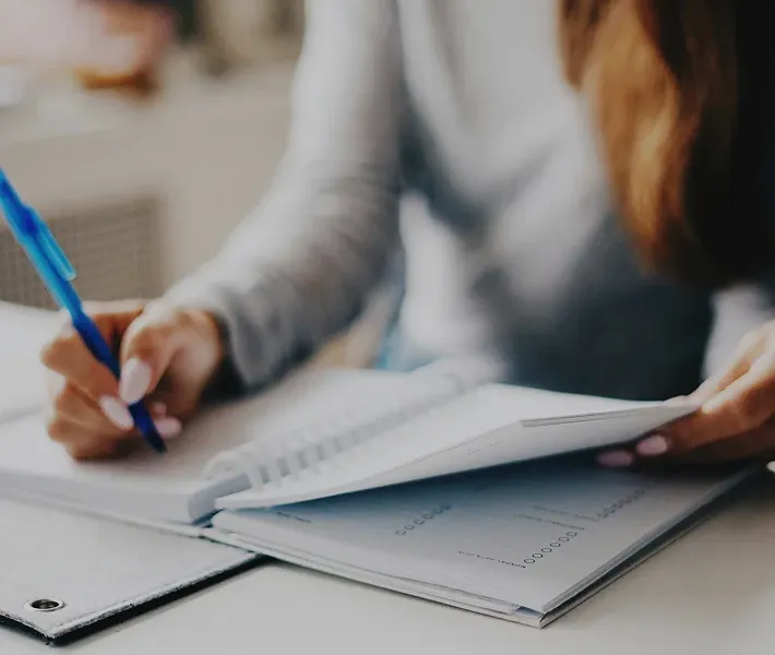 Close-up of hands writing in a notebook next to paper documents on desk