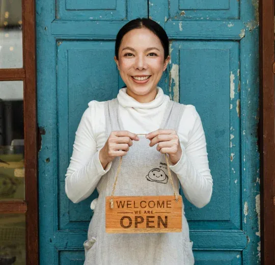 Small business owner standing at the entrance holding a “Welcome, We Are Open” sign